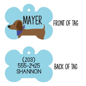 May include: A blue bone-shaped dog tag with a brown dachshund wearing a blue bandana on the front. The back of the tag has the text (203) 555-2425 SHANNON.