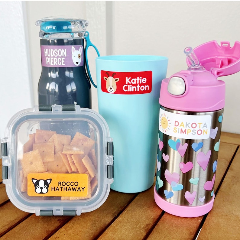 Puede incluir: Un conjunto de cuatro etiquetas personalizadas para diferentes recipientes. Las etiquetas presentan una variedad de dise&ntilde;os, que incluyen un perro, un ciervo, un sol y corazones. Las etiquetas est&aacute;n impresas con nombres y apellidos, como "Hudson Pierce", "Katie Clinton", "Dakota Simpson" y "Rocco Hathaway".