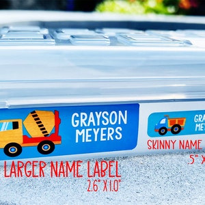 Op de afbeelding: Twee gepersonaliseerde naamstickers met een blauwe achtergrond en een ontwerp van een bouwtruck. Het grotere label is 2,6 inch bij 1,0 inch en het kleinere label is 0,5 inch bij 1,75 inch.