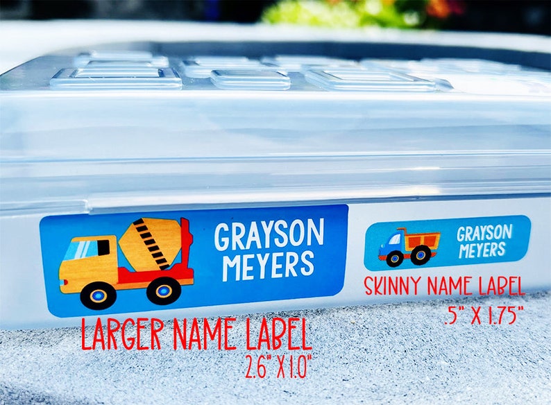 Op de afbeelding: Twee gepersonaliseerde naamstickers met een blauwe achtergrond en een ontwerp van een bouwtruck. Het grotere label is 2,6 inch bij 1,0 inch en het kleinere label is 0,5 inch bij 1,75 inch.