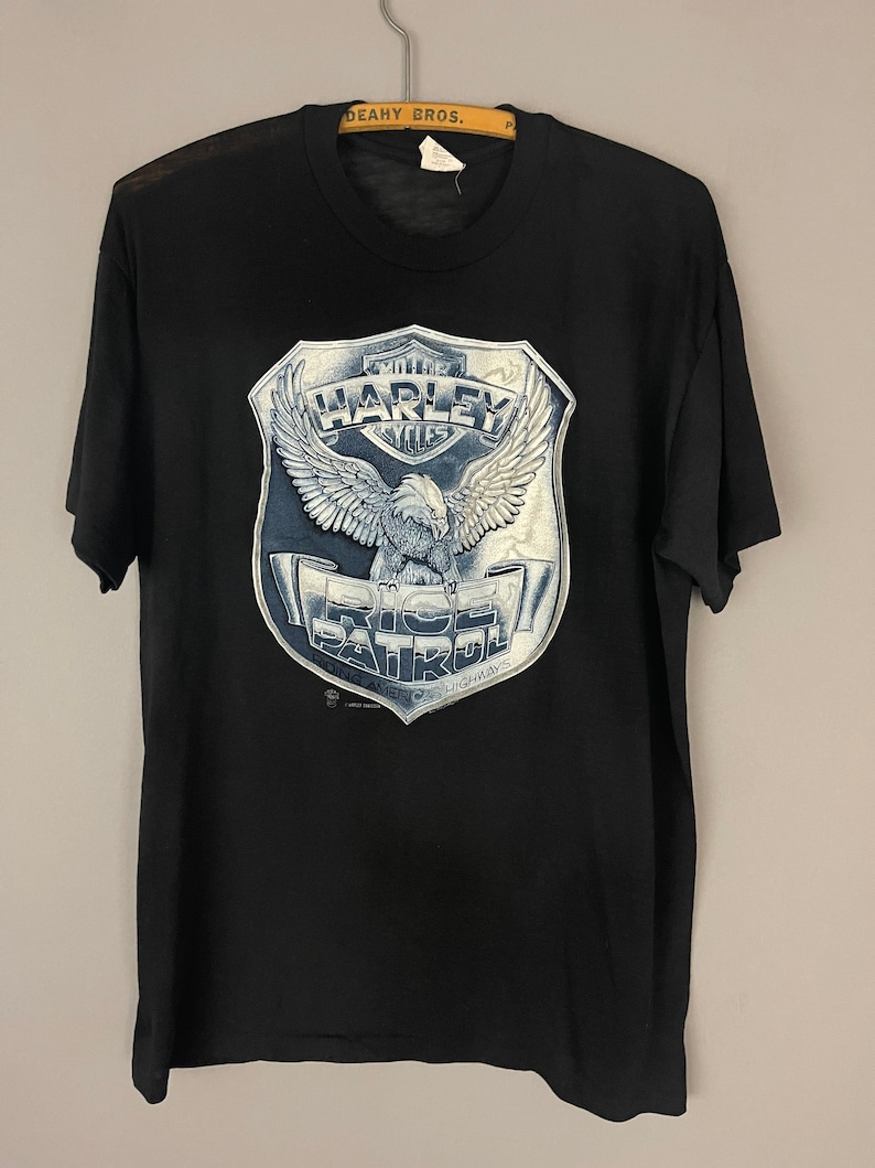May include: Black t-shirt with a white graphic of an eagle holding a Harley Davidson logo with the text "Ride Patrol" and "Rolling America's Highways".
