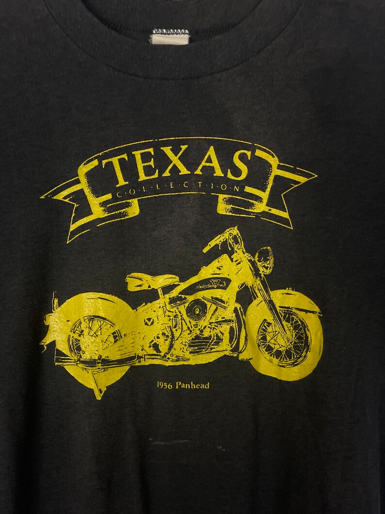 Puede incluir: Camiseta negra con un gr&aacute;fico amarillo de una motocicleta Panhead de 1956. El gr&aacute;fico incluye el texto "Texas Collection".