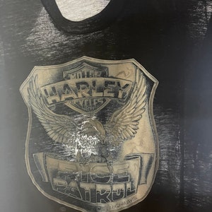 May include: Black t-shirt with a faded, silver graphic of a Harley Davidson motorcycle emblem with an eagle and the text "MOTOR HARLEY CYCLES" and "RICE PATROL" with the text "RICE HIGHWAYS" below.