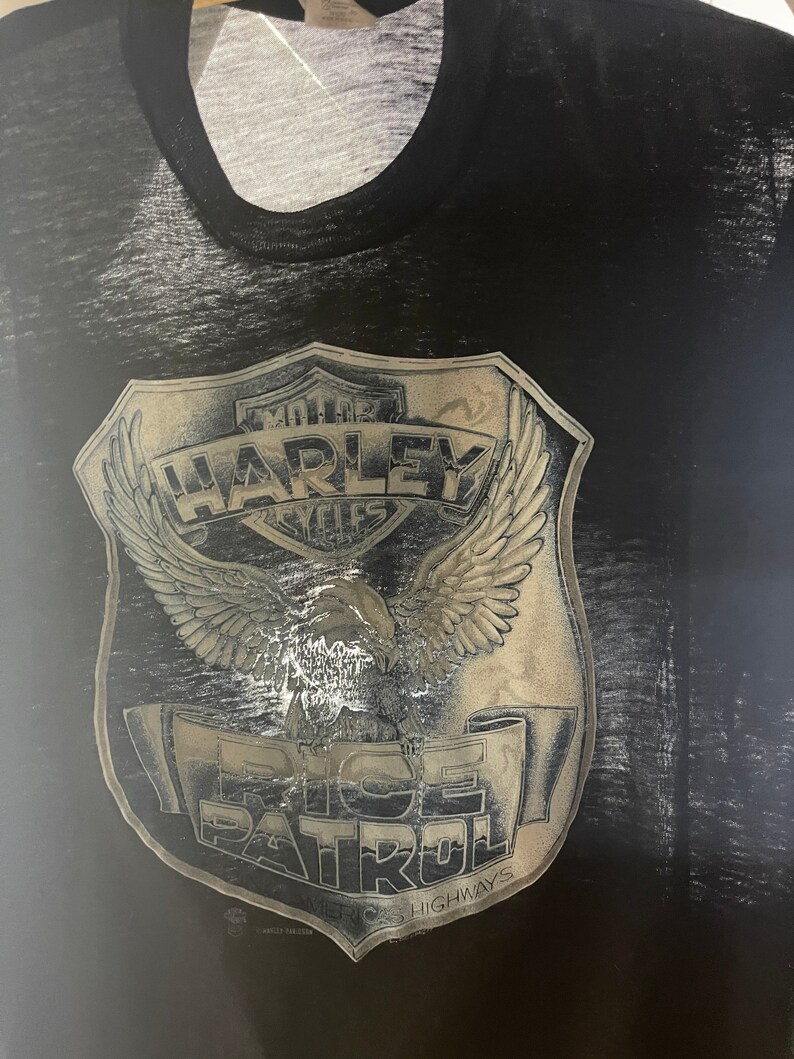 May include: Black t-shirt with a faded, silver graphic of a Harley Davidson motorcycle emblem with an eagle and the text "MOTOR HARLEY CYCLES" and "RICE PATROL" with the text "RICE HIGHWAYS" below.