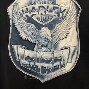 May include: A black t-shirt with a white and gray Harley Davidson logo and an eagle with wings spread. The text "Ride Patrol" is written on a banner below the eagle. The text "Riding Americas Highways" is written below the banner.