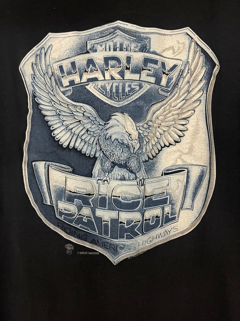 May include: A black t-shirt with a white and gray Harley Davidson logo and an eagle with wings spread. The text "Ride Patrol" is written on a banner below the eagle. The text "Riding Americas Highways" is written below the banner.