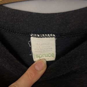 Puede incluir: Una etiqueta negra con costuras blancas, que dice "X-Large", "50% Algod&oacute;n", "50% Poli&eacute;ster", "Para el cuidado, consulte el reverso", y "spruce" en letras verdes. La etiqueta est&aacute; hecha en los Estados Unidos.