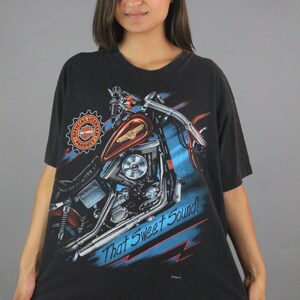 Puede incluir: Camiseta negra con un gr&aacute;fico de una motocicleta Harley Davidson y el texto "That Sweet Sound!" La camiseta tiene un logotipo Harley Davidson naranja y rojo en el lado izquierdo.