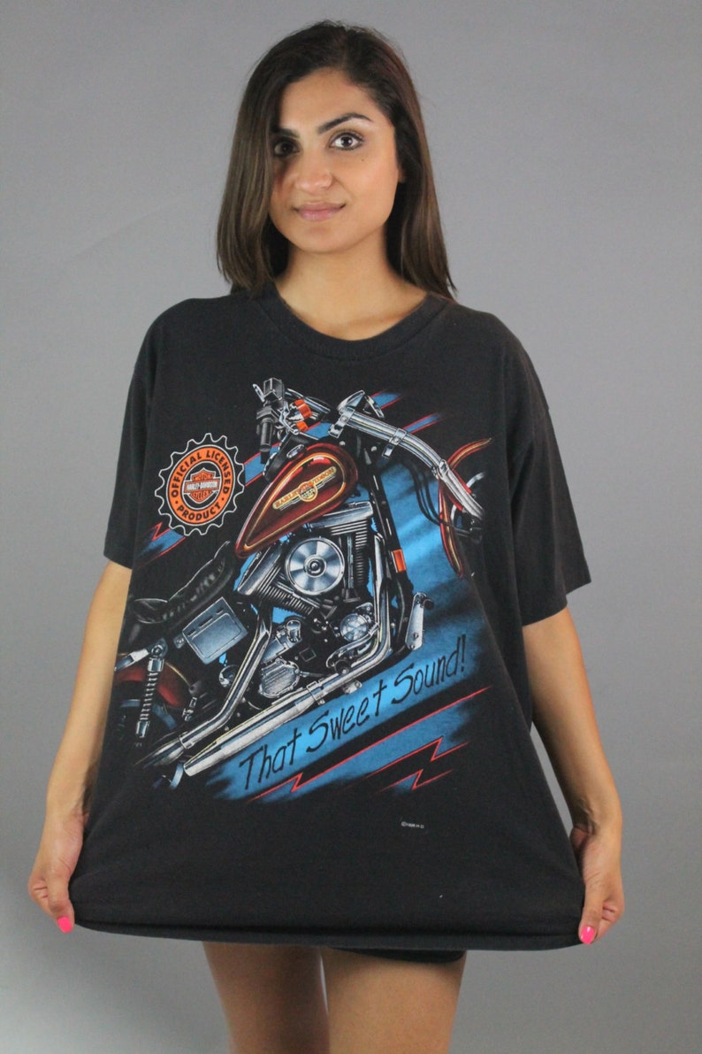 Puede incluir: Camiseta negra con un gr&aacute;fico de una motocicleta Harley Davidson y el texto "That Sweet Sound!" La camiseta tiene un logotipo Harley Davidson naranja y rojo en el lado izquierdo.