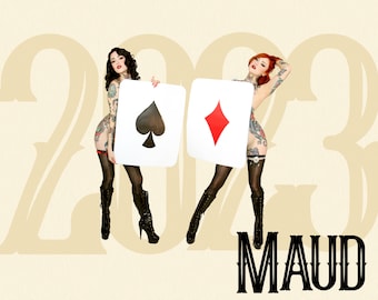 May include: Two individuals with tattoos wearing black stockings and high-heeled boots, each holding a large white card featuring a black spade or a red diamond symbol. The background displays the year 2023 and the text MAUD in black lettering.
