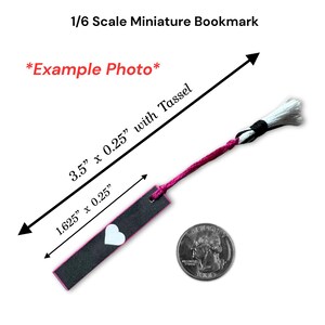 May include: A miniature bookmark, 3.5" long with a tassel, is shown next to a quarter for scale. The bookmark is black with a pink border and a white heart. The text "1/6 Scale Miniature Bookmark" and "*Example Photo*" are visible.