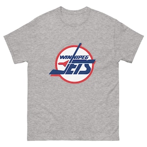 Puede incluir: Una camiseta gris jaspeado con el logotipo de los Jets de Winnipeg. El logotipo es un diseño circular con las palabras "Winnipeg Jets" en blanco y azul, con un contorno rojo. La camiseta está hecha de un material suave y cómodo.