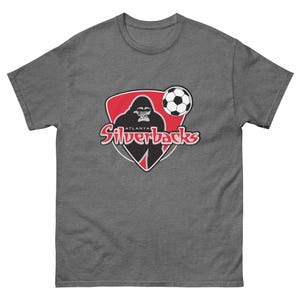 Puede incluir: Camiseta gris con el logo de los Atlanta Silverbacks. El logo incluye una silueta de gorila negro, un balón de fútbol y el nombre del equipo en rojo y blanco. La camiseta está hecha de un material suave y cómodo.