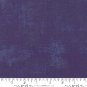 May include: A deep purple fabric featuring a mottled, textured surface pattern with subtle variations in color intensity. A white ruler is visible at the bottom edge, showing measurements in inches from 0 to 6. The text moda appears twice.
