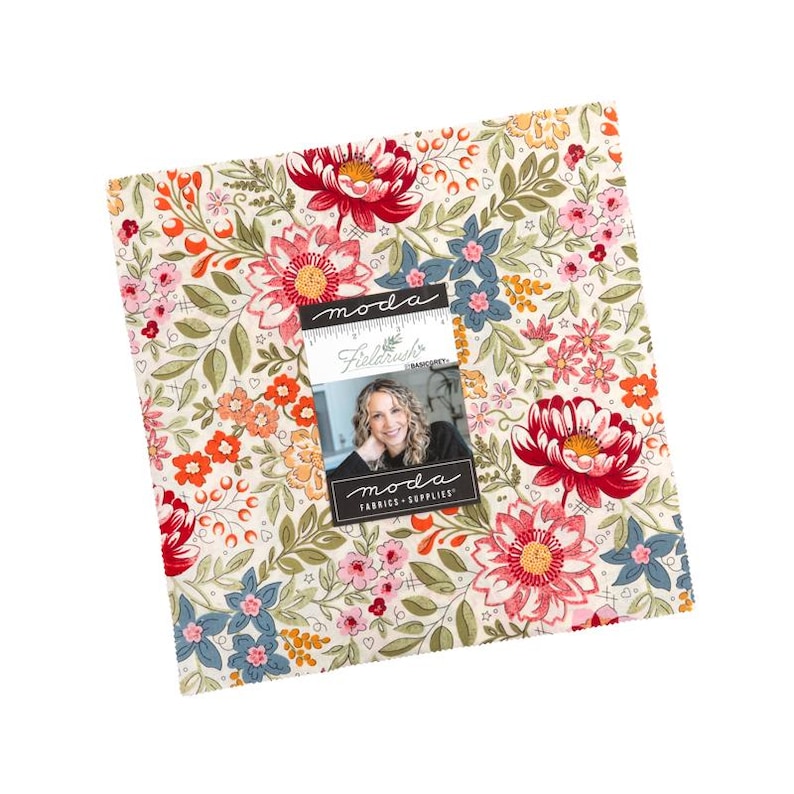 May include: A square stack of fabric squares featuring a floral pattern with red, pink, orange, and blue flowers on a cream background. A label on the front displays the text "moda", "Fieldrush", and "moda FABRICS + SUPPLIES" with a photo of a person.
