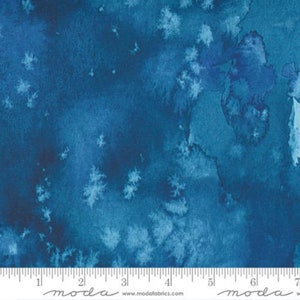 May include: A blue watercolor fabric with a white speckling pattern. The fabric has a subtle gradient from a darker blue to a lighter blue. The fabric is measured with a ruler in inches.