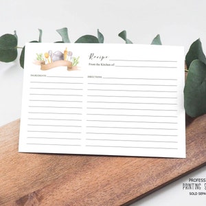 Op de afbeelding: Een blanco receptkaart met een aquarel-illustratie van keukengerei en een banner met de tekst "Recept". De kaart heeft lijnen om ingredi&euml;nten en instructies op te schrijven. De tekst "Uit de keuken van..." staat op de kaart gedrukt.
