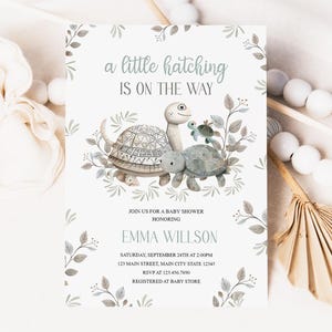 Może przedstawiać: Zaproszenie na baby shower z akwarelową ilustracją dwóch żółwi. Tekst brzmi "a little hatching is on the way" i zawiera imię "Emma Willson".