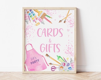 Puede incluir: Un cartel rosa con el texto "Cards & Gifts" en blanco. El cartel está decorado con ilustraciones de acuarela de pinceles, pintura y un delantal rosa con el texto "Let's Party".