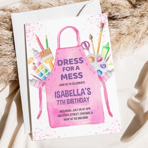 Op de afbeelding: Roze uitnodiging met een aquarel-illustratie van een roze schort met kwasten, verfbuizen en een palet. De tekst luidt "Dress for a Mess" en "Isabella's 7th Birthday".