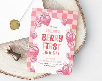 Può includere: Un invito di compleanno rosa e bianco con illustrazioni di fragole e fiori. Il testo recita "Berry First Birthday" con i dettagli dell'evento. L'invito è su una superficie di legno con una busta e un sigillo di cera dorata.