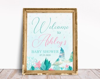 May include: A light blue and pink welcome sign with a mermaid tail design. The sign says "Welcome to Ashley's Baby Shower 07.25.2020".