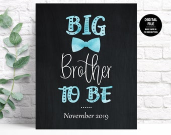 May include: A black chalkboard sign with the text "Big Brother to Be" in white script. The text "Big" is in blue with white stars and the text "to Be" is in blue with white hearts. A blue bow tie is above the text "Brother". The date "November 2019" is at the bottom of the sign.
