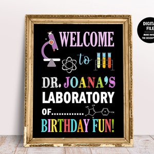 May include: A black chalkboard sign with a gold frame, announcing "Welcome to Dr. Joana's Laboratory of Birthday Fun!" with colorful text and illustrations of a microscope, test tubes, and a chemical formula.