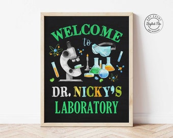Może przedstawiać: Czarna tablica z zieloną ramą, witająca gości w "Laboratorium Dr. Nicky'ego". Tablica przedstawia kreskówkowe mikroskop, zlewki i inne ilustracje o tematyce naukowej.
