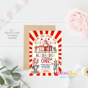 May include: A red and white striped circus tent with a yellow star and the words "Come One Come All" on the front. The tent is surrounded by colorful balloons and a clown holding a red and white striped ball. The text "Alexander is turning one" is printed in yellow and black letters. The invitation is for a birthday party on Saturday, August 7th from 2:00 to 5:00 PM. The address is 1234 Your Address, City, State 12345.