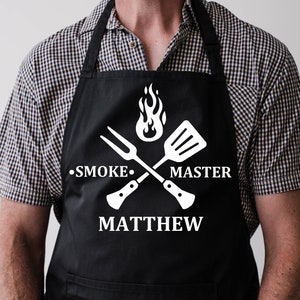 May include: Black apron with a white design of crossed grilling tools, a flame, and the text "Smoke Master Matthew".