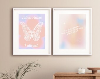 May include: Two white-framed wall art prints featuring pastel gradient backgrounds. The left print displays a white butterfly illustration with the text I dont chase I attract. The right print features the text I AM BECOMING THE BEST VERSION OF MYSELF.