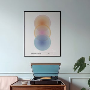 May include: A modern living room scene featuring a wooden record player on a matching cabinet. Above, a framed abstract art print with overlapping circles in orange, pink, and blue. A Monstera plant adds a touch of nature.