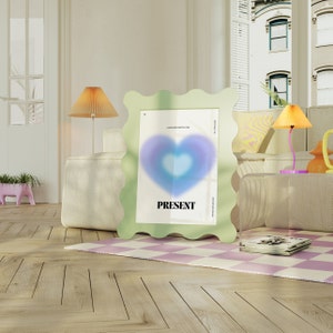 May include: A light green wavy frame with a white poster inside. The poster has a blue and purple heart with the word "PRESENT" printed below it. The frame is sitting on a white couch with a checkered rug in front of it.