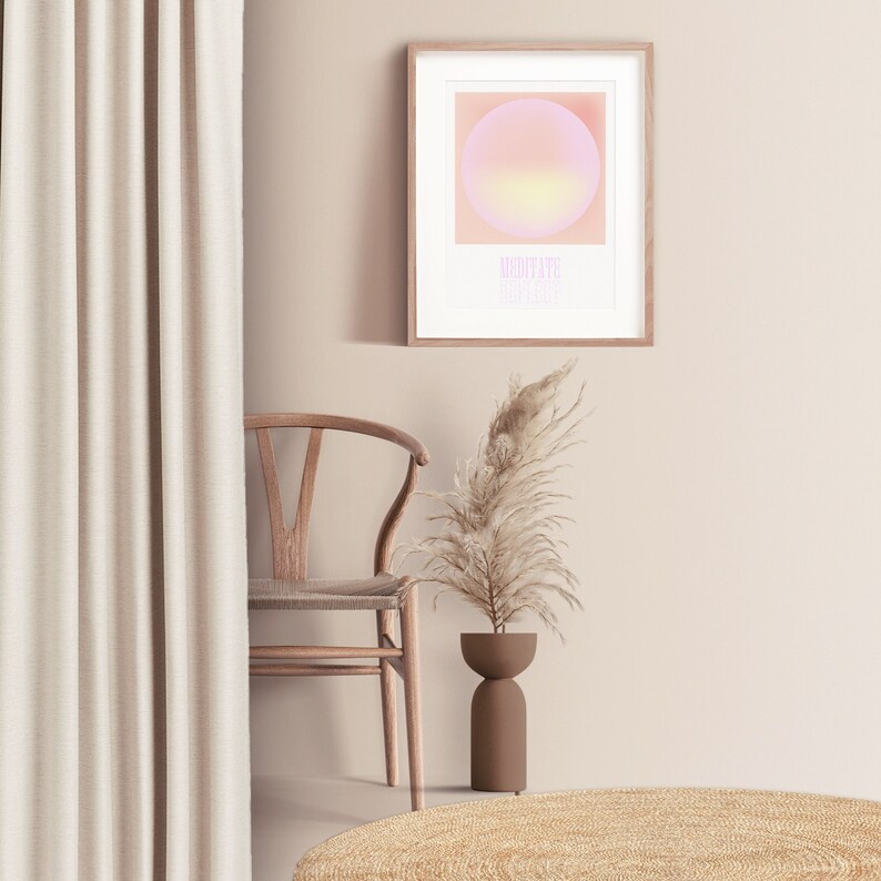 Puede incluir: Una l&aacute;mina de arte mural enmarcada que presenta un c&iacute;rculo con degradado rosa y amarillo suave sobre el texto "MEDITATE REFLECT" en una fuente rosa claro. La obra se muestra en un marco de madera clara, colgada en una pared de color neutro.