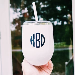 Könnte beinhalten: Ein weißer Edelstahlbecher mit einem schwarzen Monogramm "KBD" auf der Vorderseite. Der Becher hat einen Deckel und einen Strohhalm.