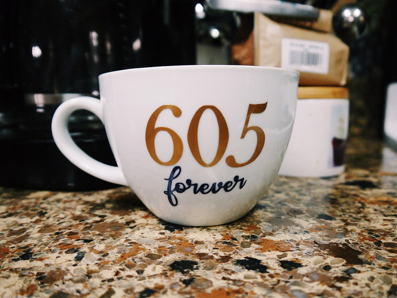 May include: White ceramic coffee mug with gold lettering that reads "605 forever".