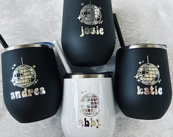 May include: Four black and white stainless steel tumblers with a silver disco ball design and personalized names: Andrea, Josie, Katie, and Abby.