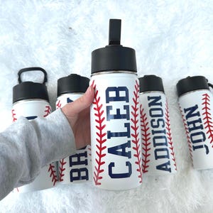 May include: White water bottles with black lids and baseball stitching designs. The bottles feature names in navy blue: CALEB, ADDISON, and JOHN. The bottles are designed to look like baseballs.
