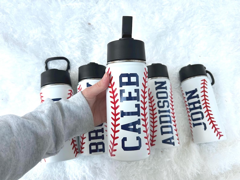 May include: White water bottles with black lids and baseball stitching designs. The bottles feature names in navy blue: CALEB, ADDISON, and JOHN. The bottles are designed to look like baseballs.