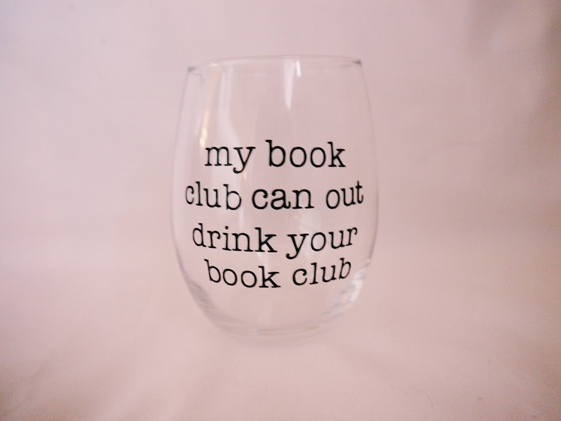May include: A clear glass wine glass with the text "my book club can out drink your book club" printed on the side.