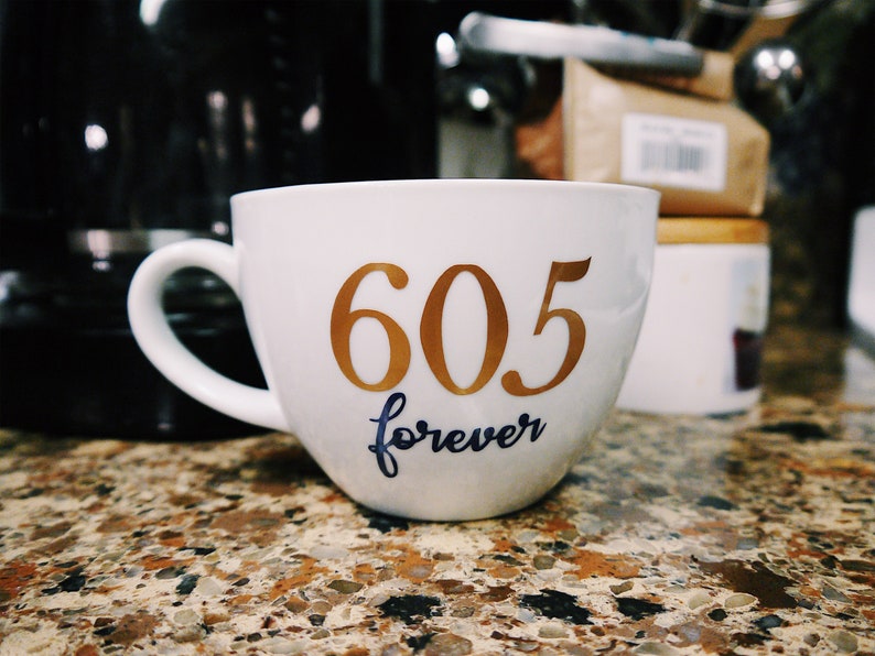 May include: White ceramic coffee mug with gold lettering that reads "605 forever".