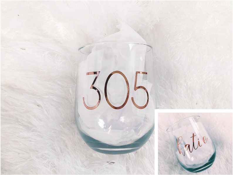 May include: Two clear glass wine glasses with gold lettering. One glass says "305" and the other says "Katie".
