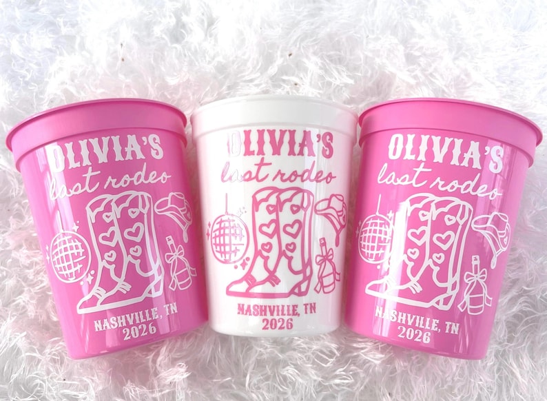 May include: Three plastic cups, two pink and one white, with a rodeo theme. The cups feature the text "OLIVIA'S last rodeo" and a graphic of cowboy boots, a disco ball, and a cowboy hat. The text "NASHVILLE, TN 2026" is also included.