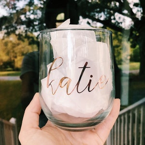 May include: A clear glass wine tumbler with the name "katie" written in gold lettering.