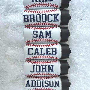 May include: Six white insulated water bottles with black lids, each featuring a baseball design. The names "NIKO", "BROOCK", "SAM", "CALEB", "JOHN", and "ADDISON" are printed in navy blue, with red baseball stitching.