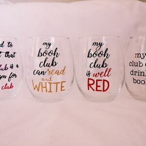 May include: Four clear wine glasses with black text and colored accents. The glasses say "delighted to find out that book club is a euphemism for wine club", "my book club can read and WHITE", "my book club is well RED", and "my book club can out drink your book club".