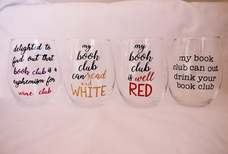 May include: Four clear wine glasses with black text and colored accents. The glasses say "delighted to find out that book club is a euphemism for wine club", "my book club can read and WHITE", "my book club is well RED", and "my book club can out drink your book club".