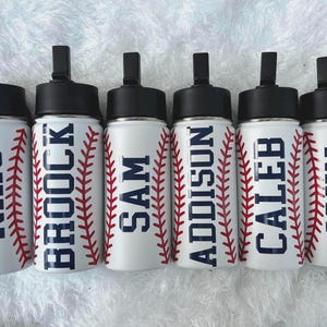 May include: Six white water bottles with black lids and the names NIKO, BROCK, SAM, ADDISON, CALEB, and JOHN in navy blue. Each bottle has a red baseball stitch design on the sides.