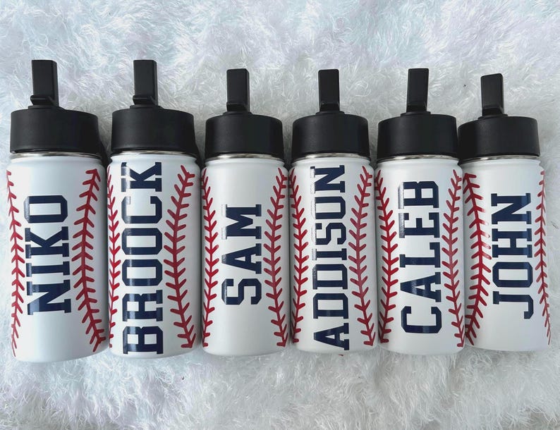 May include: Six white water bottles with black lids and the names NIKO, BROCK, SAM, ADDISON, CALEB, and JOHN in navy blue. Each bottle has a red baseball stitch design on the sides.